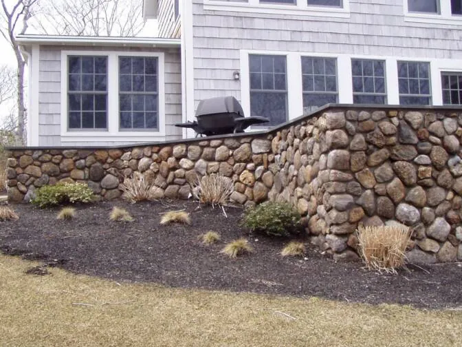 Curved fieldstone retaining wall beside a Cape Cod home