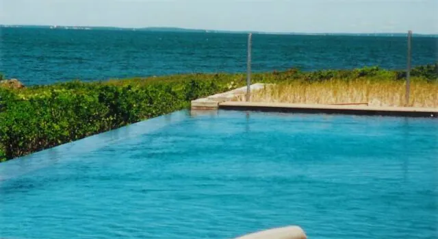 Infinity-edge pool with stone coping overlooking the water